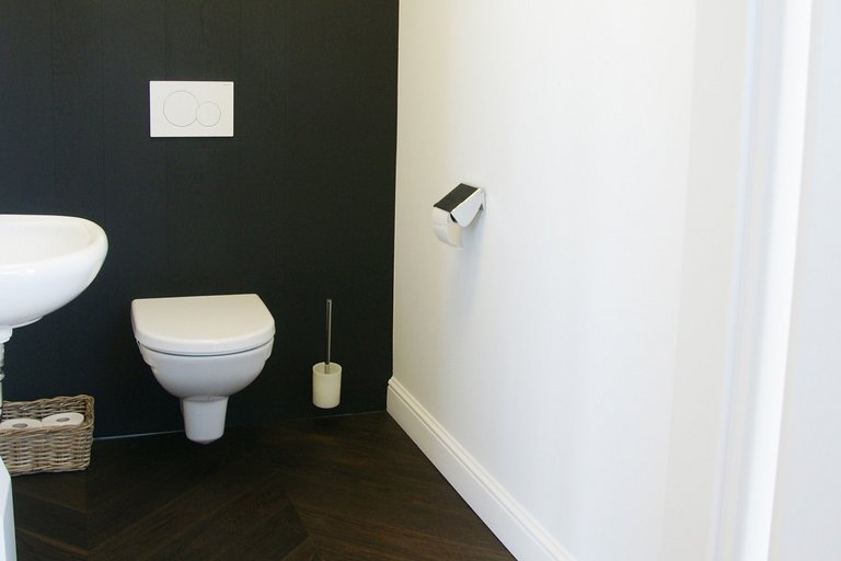 Stylish toilet with black wall and dark, smoked oak parquet flooring