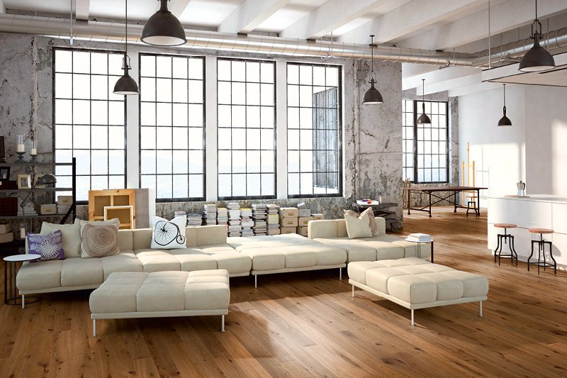 Loft apartment with industrial windows, large beige couch, and black pendant lights. The room features a country-style oak floor that creates a warm atmosphere.